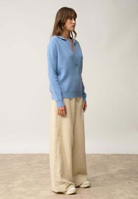 Jasnoniebieski sweter z dzianiny z kołnierzykiem, zestawiony z beżowymi spodniami o szerokich nogawkach z korduroju. Tekstury kontrastują ze sobą łagodnie pod względem koloru i stylu.