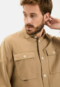 Beige lange mouwen shirt van katoen, met een knoopsluiting aan de voorkant, twee borstzakken en een kraag. Soepele textuur met een klassiek ontwerp.