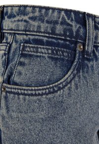 Denim jeans with a faded blue color, featuring a curved back pocket, visible stitching details, and a metal button closure.