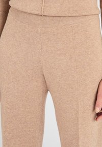 Leggings a maglia beige con una consistenza morbida, dotati di un elastico in vita aderente e dettagli delle cuciture delicati, che offrono un aspetto confortevole e slanciato.