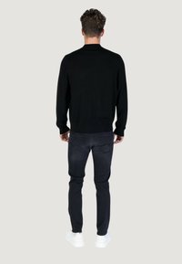 Maglione nero con scollatura rotonda, tessuto texture. Abbinato a jeans slim-fit grigi scuri e sneaker bianche. Vista da dietro.