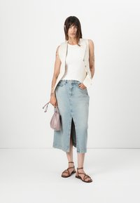 Denimsjørte i lys blått med en frontsplitt, parret med en hvit erm løs topp og en kremfarget vest. Grå veske og brune sandaler med remmer.