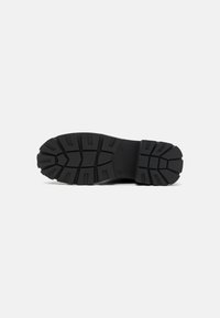 Black rubber shoe sole featuring a thick tread pattern with deep grooves for traction, flat design, and a textured surface.