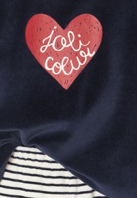 Cotton sweatshirt featuring a red heart graphic with the text "Joli Couleur" in white cursive, set against a dark blue background, layered over a striped fabric.
