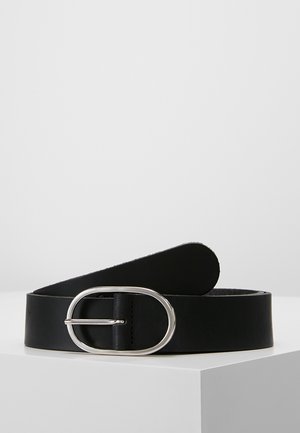 Ceinture en cuir noir avec une boucle ovale argentée reposant enroulée sur une surface blanche sur fond gris clair.