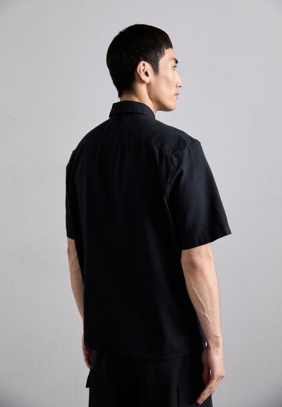 Čierna košeľa s krátkym rukávom a klasickým golierom, bavlnený materiál, rovný strih a jemné švy viditeľné na chrbte.