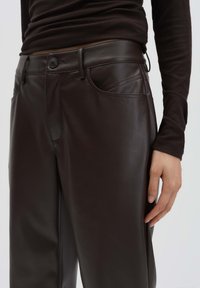 Close-up of dark brown faux leather pants with button and pockets, worn with a matching long-sleeve ribbed top.