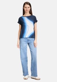 Granatowa bluzka z krótkim rękawem w białe i niebieskie abstrakcyjne wzory, połączona z jasnoniebieskimi dzwonami i białymi sneakersami. Gładka bawełniana faktura.