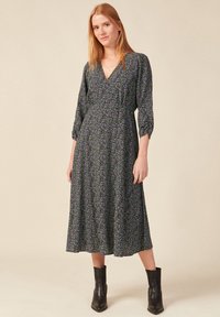 Schwarzes mittellanges Blumenkleid mit V-Ausschnitt, dreiviertelÄrmeln und gerafftem Bund. Das Muster zeigt kleine lila Blumen auf einem dunklen Hintergrund.