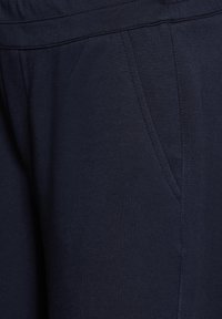 Närbild av marinblå byxor som visar sidoficka med synlig söm och midjebandets söm.