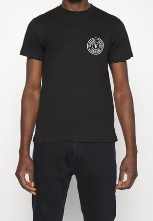 Czarna bawełniana koszulka z okrągłym dekoltem, z okrągłym białym logo po lewej stronie klatki piersiowej. Prosty design i krótkie rękawy.