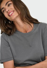 Camiseta gris de manga corta con cuello redondo, hecha de una tela suave. Presenta costuras limpias y un ajuste holgado. Textura sutil visible.