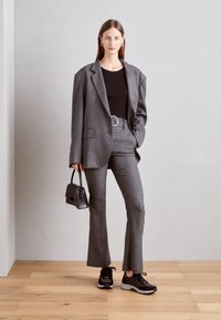 Gray plaid tailored suit with a relaxed fit blazer, flared pants, a black top, black sneakers, and a small black handbag.