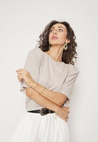 Szary T-shirt z krótkim rękawem w luźnym kroju, zestawiony z czarnym paskiem z ozdobną klamrą oraz delikatnymi bransoletkami i kolczykami.