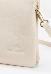 Krémová kožená crossbody taška s texturovaným povrchem, zlatou kováním, nastavitelným popruhem a raženým logem na přední straně.