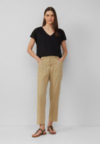 T-shirt noir à col en V avec des accents en dentelle, associé à un pantalon élastique beige clair à taille haute avec deux poches avant. Sandales plates noires.
