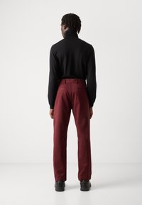 Pull en col roulé noir associé à un pantalon droit bordeaux. Le pantalon possède des poches arrière et un tissu lisse et durable. Chaussures noires.