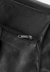 Primo piano di una borsa in pelle nera a granuli con zip argentata visibile e dettagli cuciti sulla superficie testurizzata.