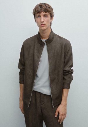 Brown bomber jacket with a high collar, made of textured fabric, paired with a light gray crew-neck shirt and matching pants.