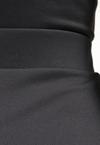 Musta kangas, jolla on sileä rakenne, varustettuna tiukalla muotoilulla ja näkyvillä saumoilla. Huomio keskittyy kankaan tasaisiin, mattaiseen pintaan.