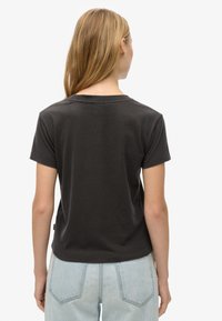 T-shirt in cotone nero con maniche corte, scollatura rotonda e vestibilità rilassata. Presenta un orlo dritto e una marcatura minimalista sul lato.