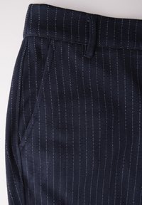 Marineblauwe stoffen broek met dunne witte streepjes, een platte tailleband, zijzakken en een soepele textuur.