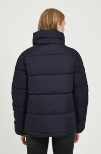 Doudoune marine avec un col haut, un design matelassé et des poignets élastiques, présentant une texture lisse et une finition légèrement brillante.