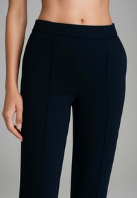 Pantaloni a vita alta di colore navy in tessuto liscio, caratterizzati da due pieghe frontali e una cintura larga, progettati per una vestibilità su misura.