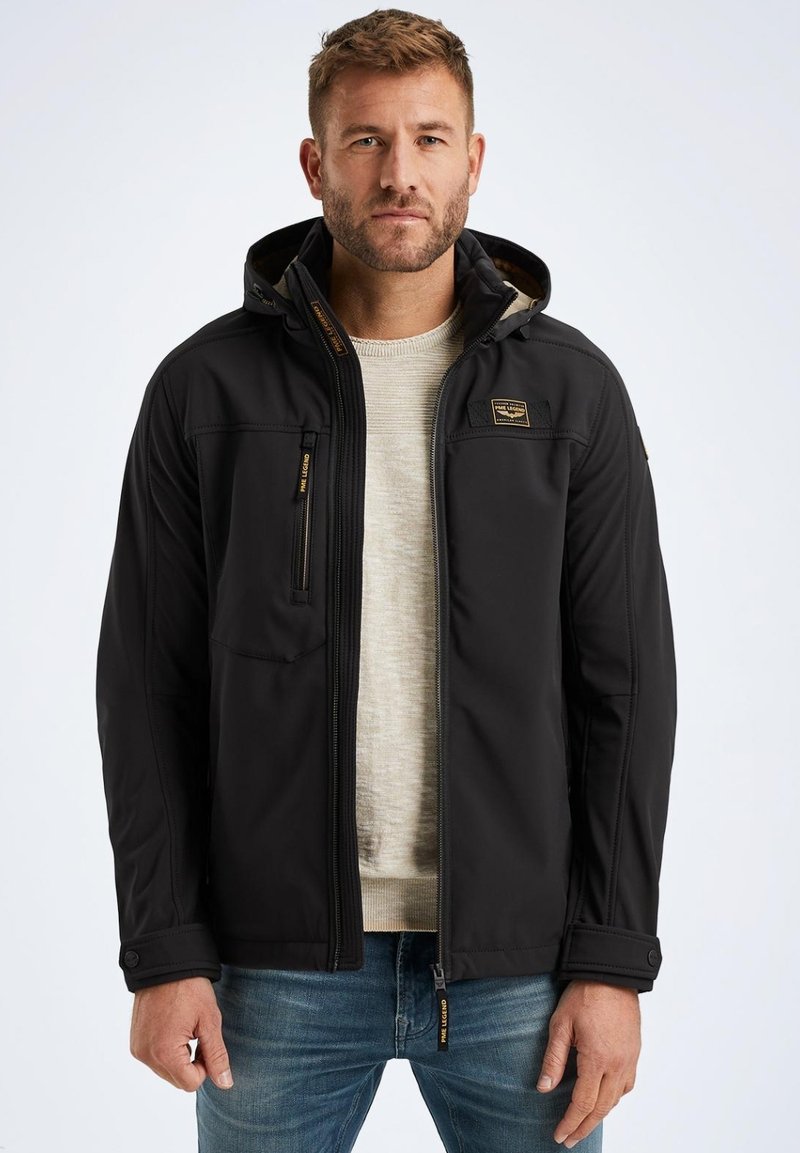 Black softshell jacket with a zippered front, hood, and pockets. Features a smooth texture, detailed stitching, and a logo patch on the chest.