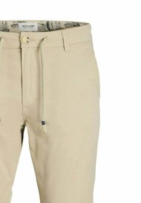 Pantaloni beige realizzati in tessuto di cotone, con chiusura a bottone, vita con cordino e fodera interna con motivo.