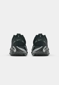 Pár čiernych a sivých bežeckých tenisiek Nike zobrazených zozadu na bielom pozadí.