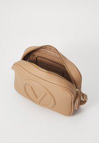 Sac crossbody en cuir tan avec logo 'V' en relief, finition texturée, fermeture éclair dorée et poche intérieure. Forme rectangulaire compacte.