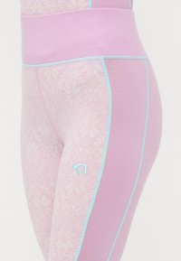 Närbild av lavendel- och ljusrosa leggings med snöflingemönster, ljusblå sömmar, hög midja och liten broderad logotyp på låret.