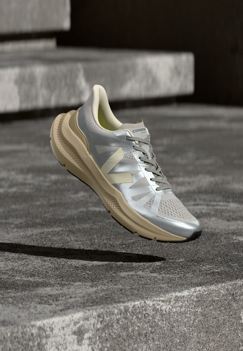 Ασημί και μπεζ παπούτσι για τρέξιμο με υφή στην σόλα, κορδόνια και σήμανση, αιωρούμενο πάνω από τραχύ σκυρόδεμα και σκαλοπάτια.