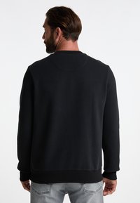 Felpa nera con maniche lunghe, colletto tondo e polsini a coste. Tessuto morbido con una texture liscia, caratterizzata da un design semplice e privo di decorazioni.