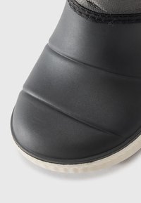 Botte noire imperméable avec une tige texturée, un embout côtelé et une semelle en caoutchouc blanche. Le design est élégant et minimaliste, adapté aux conditions humides.