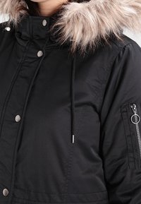 Černá zateplená bunda s kapucí lemovanou kožešinou, patentkami, zipovou kapsou na rukávu a nastavovacími šňůrkami u krku.