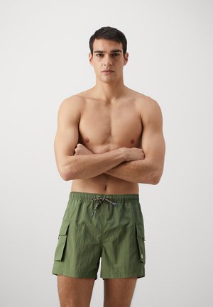 Pantaloni da bagno verdi con vita elasticizzata e cordino, dotati di due tasche cargo laterali e realizzati in tessuto leggero e testurizzato.
