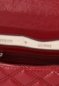 Rote, gesteppten Leder-Geldbörse mit glänzender Oberfläche. Das Innere ist mit beigem Stoff ausgekleidet und trägt das "GUESS"-Logo. Enthält ein Reißverschlussfach.