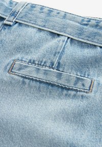 Ljust blå denimtyg med en subtil textur, med en bakficka som har en klaff säkrad med sömnad. Midjebandet har en ren finish.