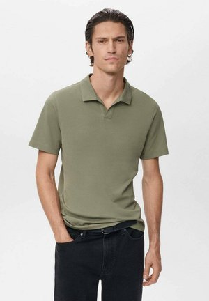Polo de color verde oliva con collar clásico y mangas cortas, hecho de una tela suave. Llevado con jeans negros y un cinturón negro.