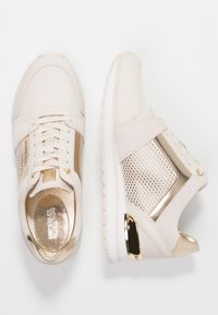 Light beige athletic shoes with gold accents, suede and mesh materials, a lace-up design, and textured panels, featuring a white sole.