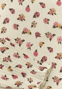 Blomsterpryttat tyg med små rosa och gula blommor och gröna blad på en krämfärgad herringbonebakgrund. Texturerad volangdetalj.