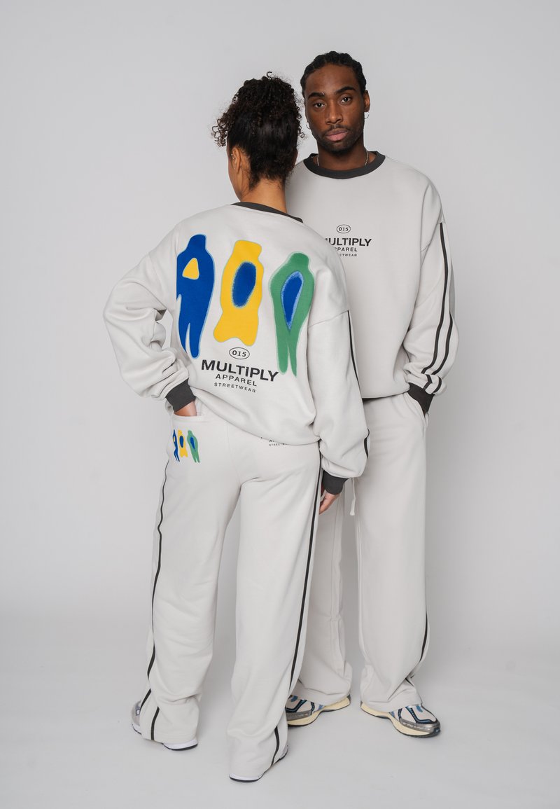 Grauer Sweatshirt und Hose mit bunten abstrakten Designs in Blau, Gelb und Grün. Verfügt über schwarze Seitenstreifen und vorderen Logotext.