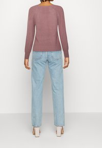 Maglione a coste di un tenue colore malva, con maniche lunghe e scollo rotondo, abbinato a jeans in denim azzurro chiaro a vita alta e scarpe con tacco bloccato beige.