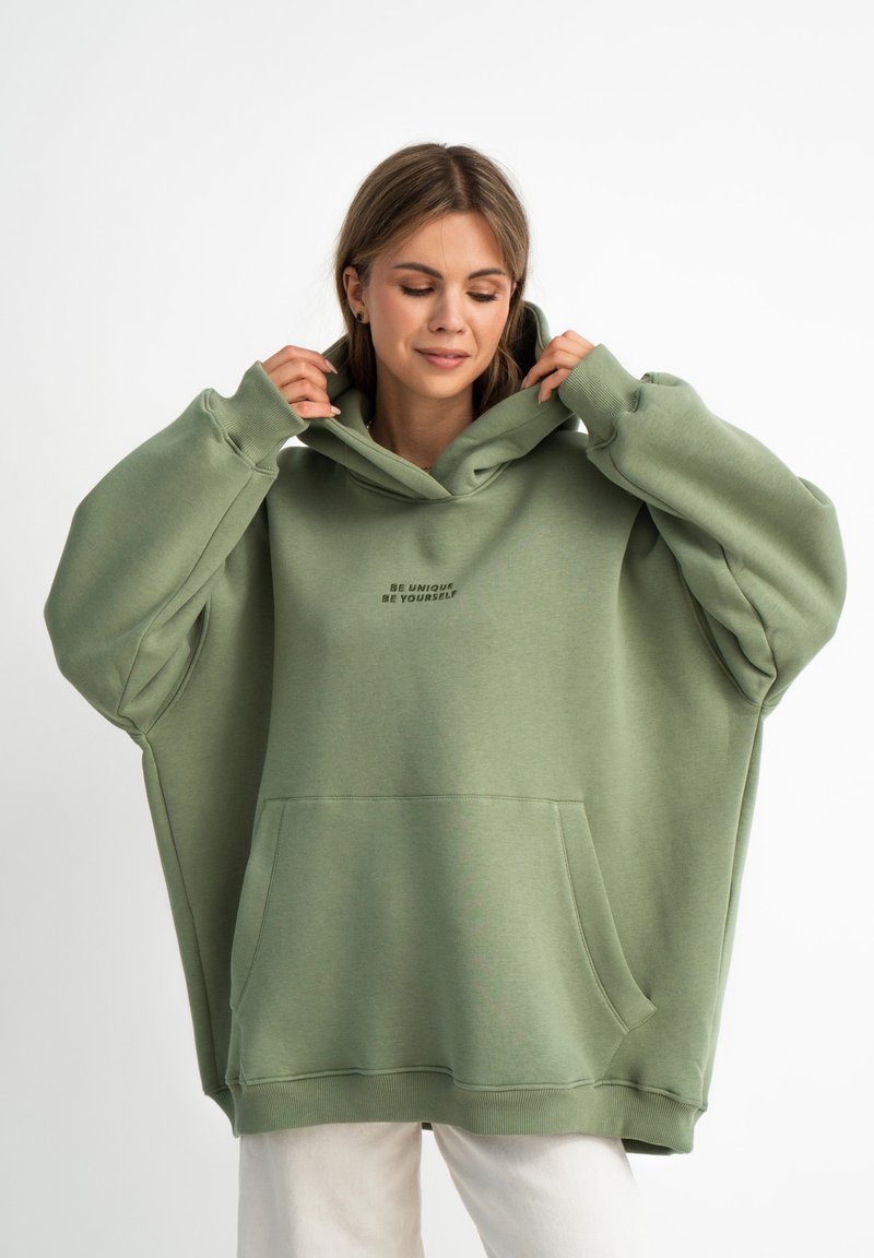 Przytulny, oversize'owy sweatshirt z kapturem w miękkim oliwkowozielonym kolorze, z przednią kieszenią oraz nadrukowanym tekstem "Bądź unikalny, bądź sobą."