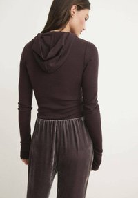 Felpa a maniche lunghe viola scuro con un design focalizzato sul retro. Presenta un cappuccio rotondo e una silhouette aderente, abbinata a pantaloni grigi morbidi e peluche.
