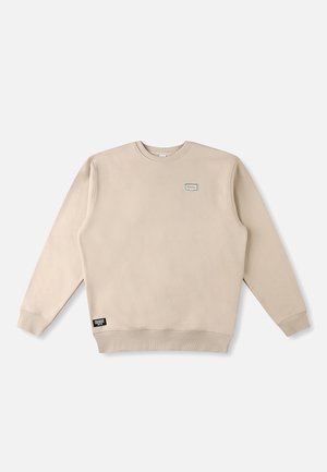 Beige crewneck-trui gemaakt van zachte stof, met een klein logopatch op de borst en een merklapje aan de onderzoom.