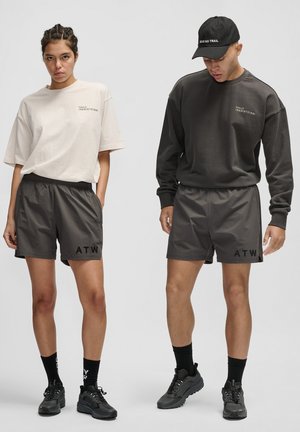 Two models wear matching casual outfits: a light beige oversized shirt and dark sweatshirt with black shorts, featuring "ATW" branding in black.