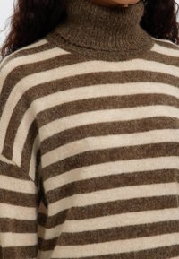 Brun och krämrandig polotröja gjord av mjukt, texturerat stickat tyg. Har ribbad krage och avslappnad passform.